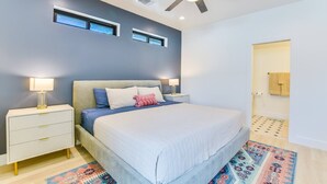 Ein modernes Schlafzimmer mit einem Bett, Nachttischen, einem Deckenventilator und einer Badezimmertür.