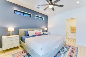 A modern bedroom with a bed, bedside tables, a ceiling fan, and a bathroom door. - Modern New Oasis w/ Private Pool & Fenced Yard (Austin)