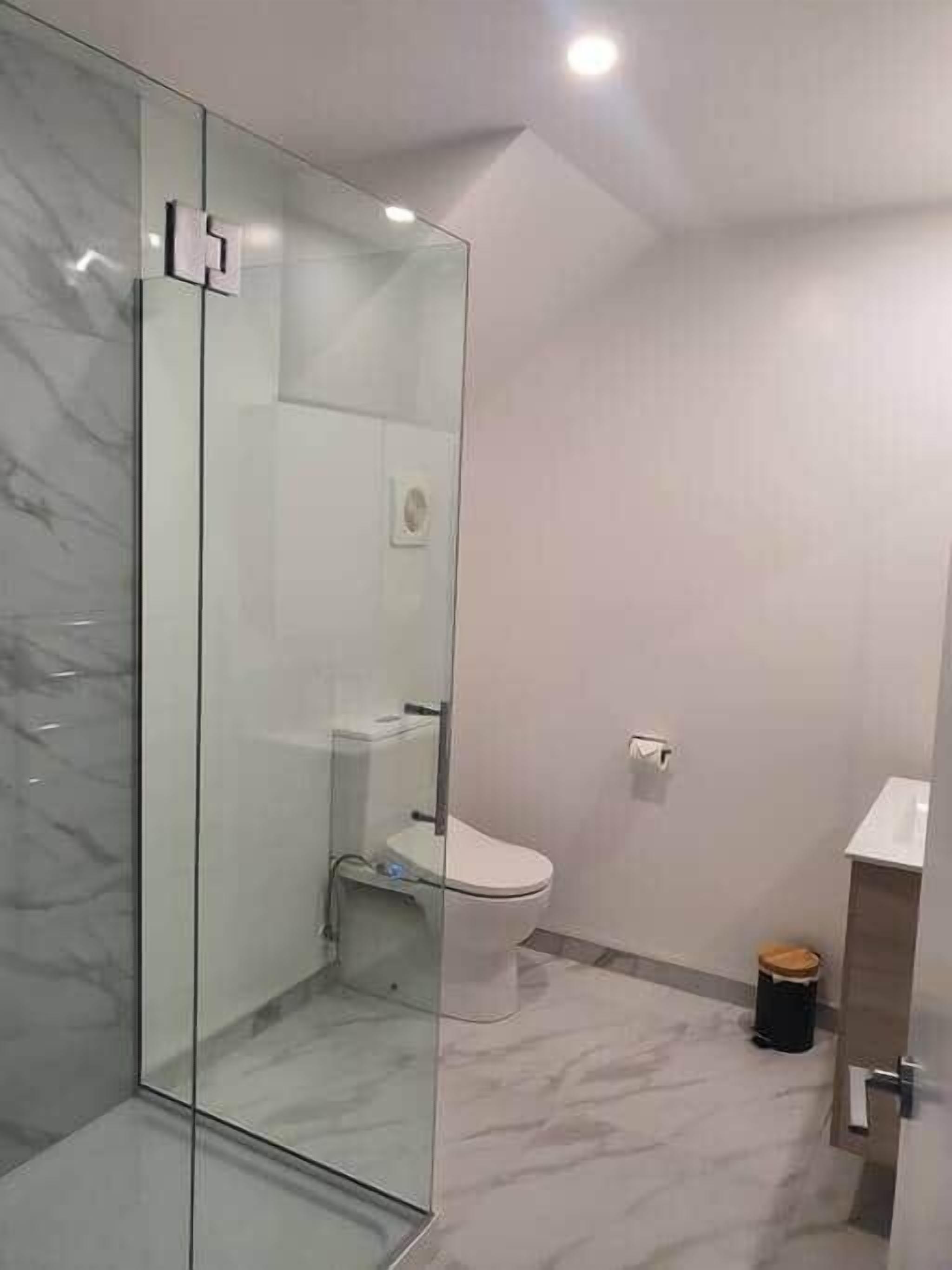 A modern bathroom with a glass shower enclosure, a toilet, and a trash bin.