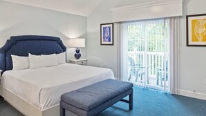 A hotel room with a large bed, a bench, a nightstand, and a window with a view of greenery.
