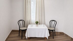 Ein Tisch für zwei Personen, zwei Stühle, ein Blumentopf und ein Fenster mit Vorhängen.