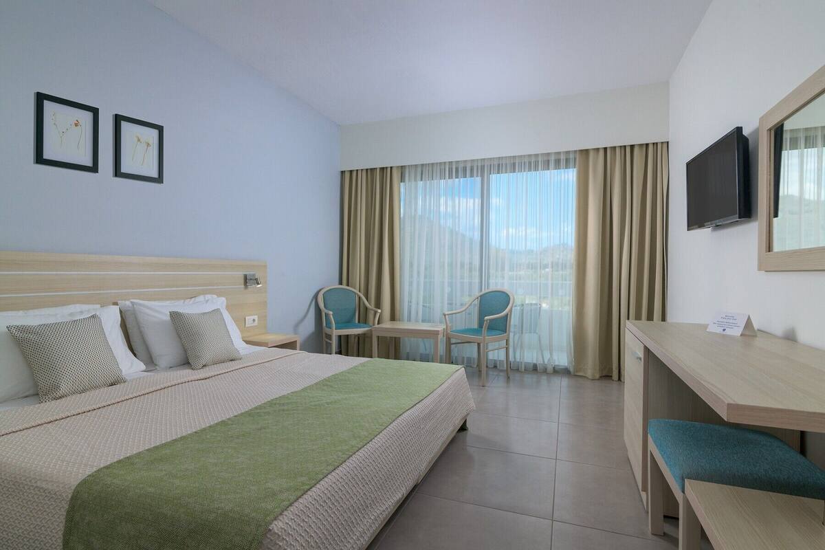 Una camera d'albergo con un letto, una scrivania, due sedie, una televisione e tende.