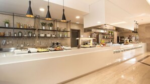 A modern kitchen with stainless steel appliances, hanging utensils, and a buffet setup. - Niriides Hotel (Rhodes)
