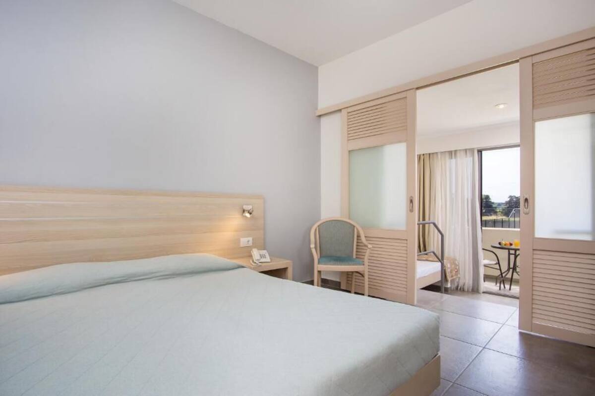 Una camera d'albergo con un letto, una sedia, un tavolino, un telefono e un balcone con vista.