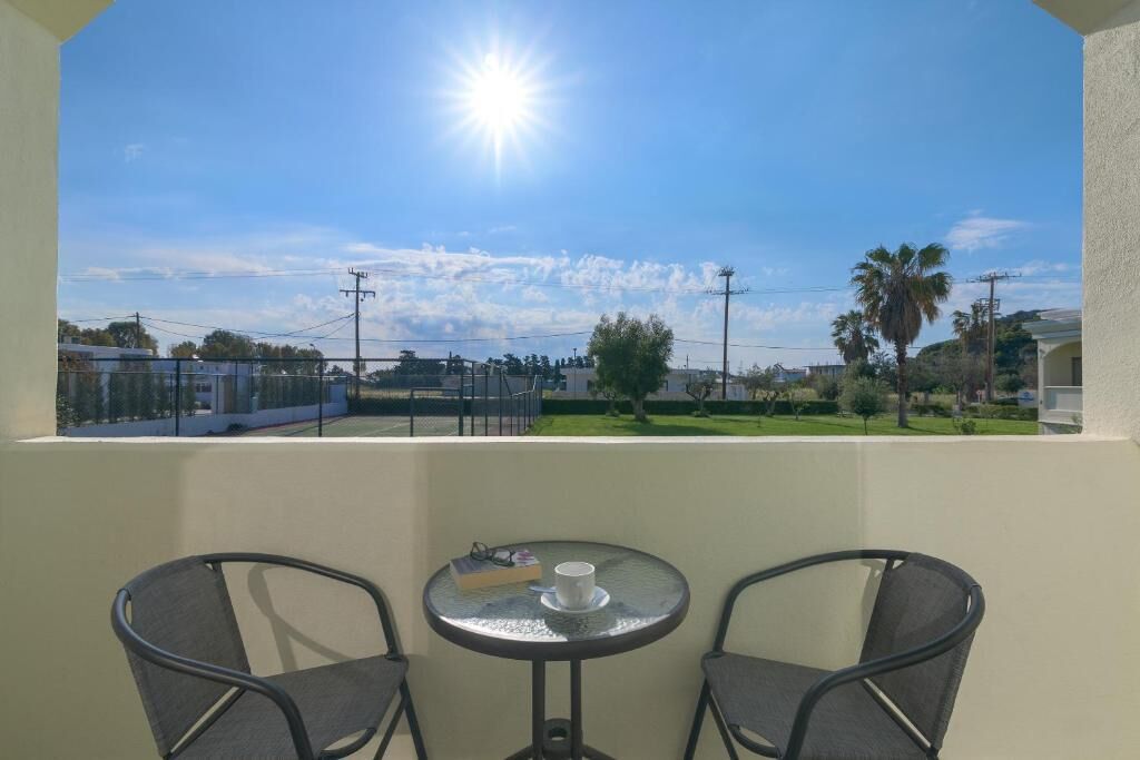 A balcony with two chairs and a table, overlooking a residential area with houses and greenery.