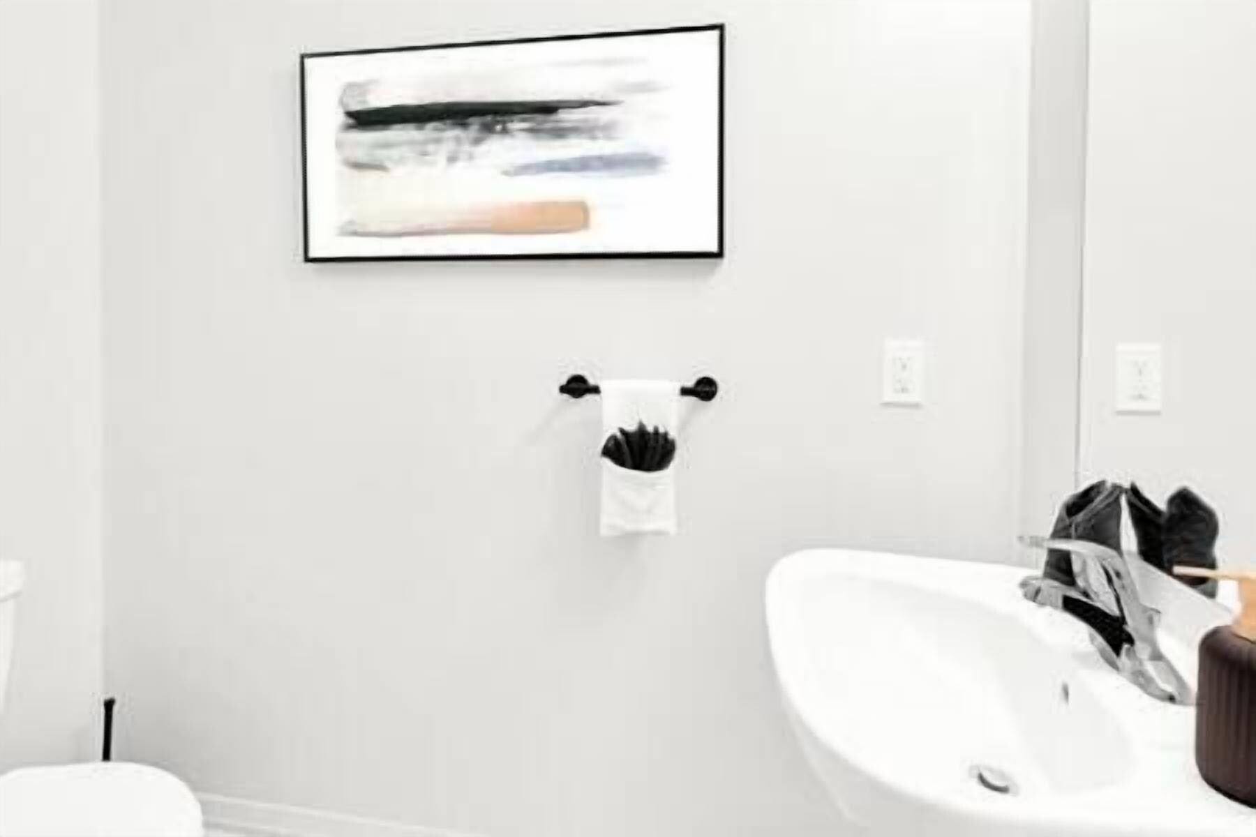 Une salle de bain avec un lavabo blanc, un tableau abstrait encadré accroché au mur et une serviette suspendue à un porte-serviettes.