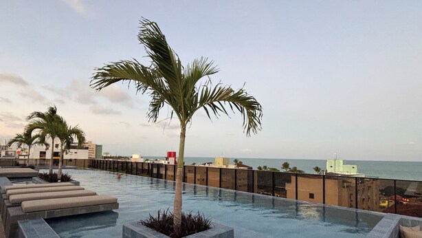 A rooftop infinity pool with a palm tree, lounge chairs, and a view of the ocean. - Apartment steps away from the beach, ideal to enjoy the Brazilian Caribbean. (João Pessoa)