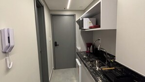 A narrow hallway leading to a kitchen with a microwave, a coffee maker, and a sink. - Apartment steps away from the beach, ideal to enjoy the Brazilian Caribbean. (João Pessoa)