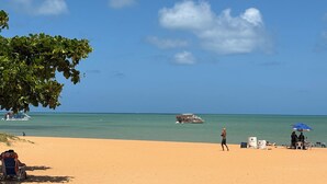 A beach with a clear sky, a boat in the water, and a person walking. - Apartment steps away from the beach, ideal to enjoy the Brazilian Caribbean. (João Pessoa)