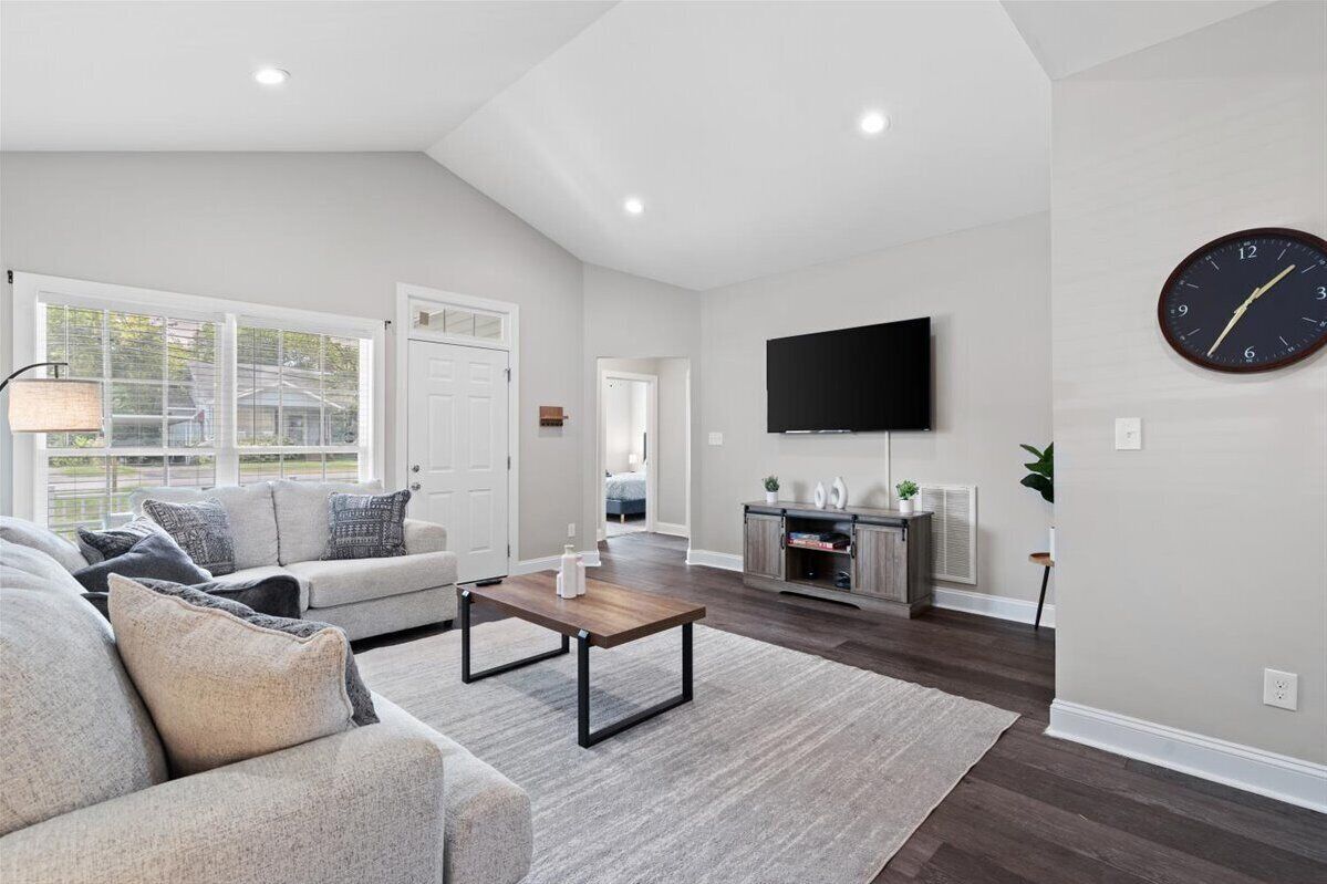 A spacious living room with a grey sofa, a wooden coffee table, and a flat-screen TV mounted on the wall.