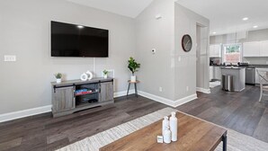 Uma sala de estar moderna com televisão de tela plana, móvel para TV em madeira e um espaço de jantar com mesa em madeira.