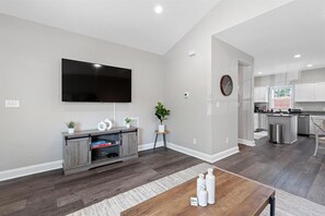 A modern living room with a flat-screen TV, wooden entertainment unit, and a dining area with a wooden table. - Charming Gastonia Escape 3BR 2BA • New Furnishings (Gastonia)
