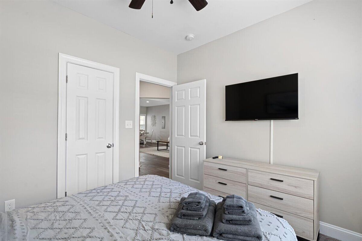 Une chambre à coucher comprenant un lit, une commode, un téléviseur et deux portes donnant sur d’autres pièces.