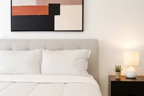 A neatly made bed with striped bedding, a headboard, and a bedside table with a lamp and a small plant. - Spa - River - Game Room | Le Belvedere (Mont-Tremblant)