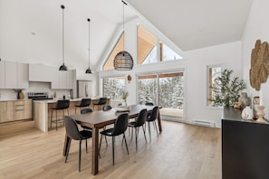 Eine moderne Küche mit Essbereich, großen Fenstern und hoher Decke.