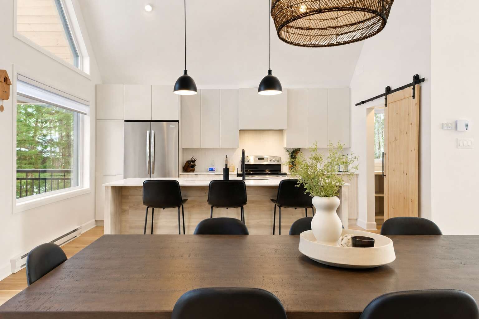 A modern kitchen with white cabinets, a central island, and a dining area with a dark wooden table and black chairs.