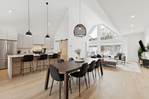 A spacious kitchen with a central island, black bar stools, and pendant lighting. - Spa - River - Game Room | Le Boréal (Mont-Tremblant)