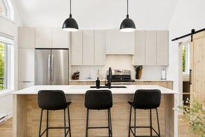 A modern kitchen with a central island, stainless steel appliances, and black bar stools. - Spa - River - Game Room | Le Boréal (Mont-Tremblant)
