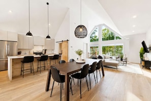 A modern kitchen with a dining area, large windows, and a high ceiling. - Spa - River - Game Room | Le Boréal (Mont-Tremblant)