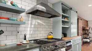 A modern kitchen with a gas stove, a stainless steel range hood, and a built-in oven. There are white tiled walls and a wooden floor. - Beachcrest Cottage in Twin Lakes Beach (Santa Cruz)