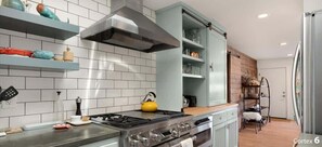 A modern kitchen with a gas stove, a stainless steel range hood, and a built-in oven. There are white tiled walls and a wooden floor. - Beachcrest Cottage in Twin Lakes Beach (Santa Cruz)