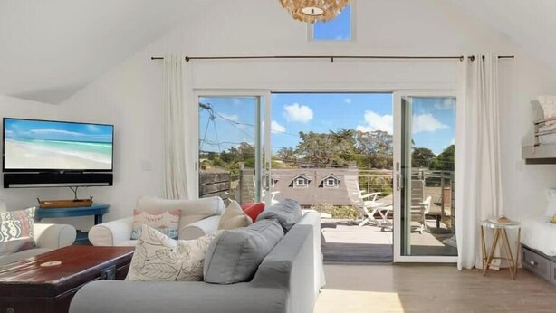 A spacious living room with a large TV, comfortable seating, and a view of the outdoors. - Beachcrest Cottage in Twin Lakes Beach (Santa Cruz)