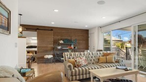 A modern living room with a sofa, armchairs, a coffee table, and a dining area with a kitchen in the background. - Beachcrest Cottage in Twin Lakes Beach (Santa Cruz)