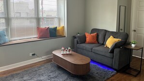 A modern living room with a grey sofa, colorful cushions, a wooden coffee table, and a window with blinds. - Ravenswood Loft - Peaceful 2-bedroom apartment in vibrant Chicago (Chicago)