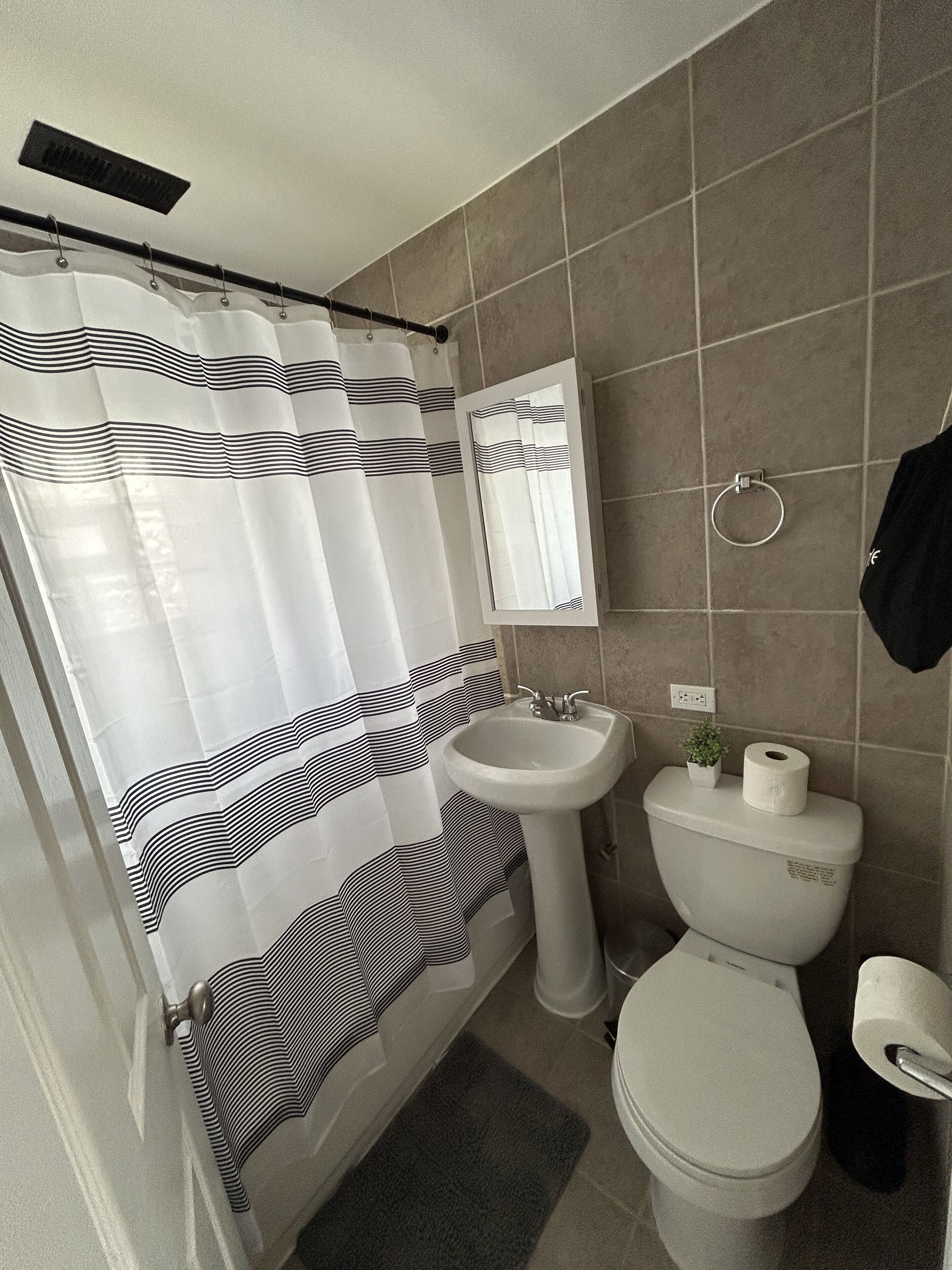 A bathroom with a shower curtain, sink, toilet, and a mirror.