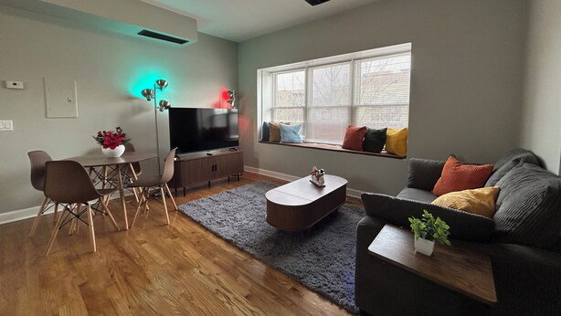 A modern living room with a flat-screen TV, a dining area with chairs, a sofa, and a window with blinds. - Ravenswood Loft - Peaceful 2-bedroom apartment in vibrant Chicago (Chicago)