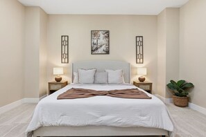 Une chambre moderne avec un grand lit, deux tables de chevet avec des lampes, une œuvre d’art accrochée au mur et une plante en pot.