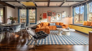 A modern living room with a sofa, coffee table, and chairs. There are large windows with curtains, a dining table with chairs, and artwork on the walls. - NEW The Cap Hill Heartbeat | Walk to Shops & Cafés (Seattle)