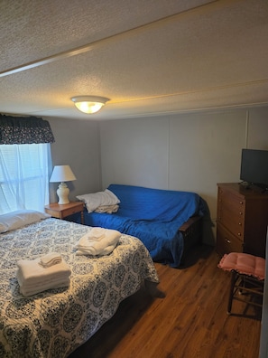 A bedroom with a bed, a dresser, a chair, a lamp, and a television.