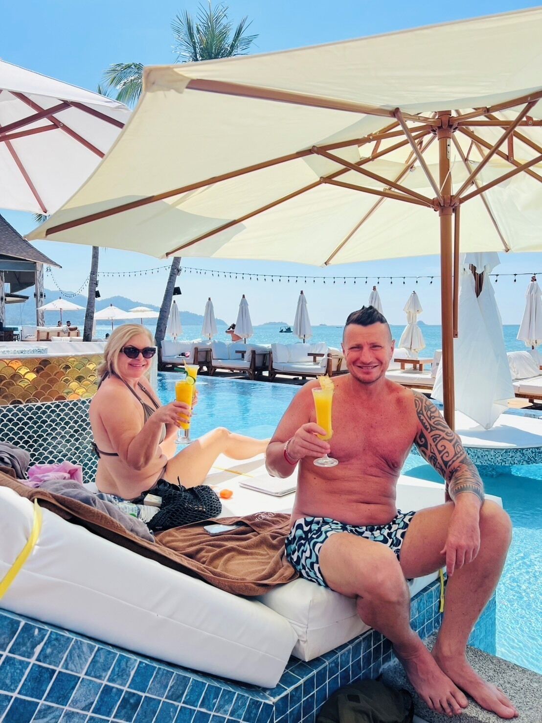 Un espace aménagé au bord de la piscine, avec des chaises longues et des parasols, une vue dégagée sur la mer et un bord de piscine revêtu de carrelage.