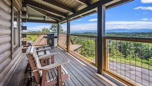 A wooden deck with picnic tables and a grill, overlooking a forested landscape. - Mountain View - Hot Tub - Game Room - Pool (Sevierville)