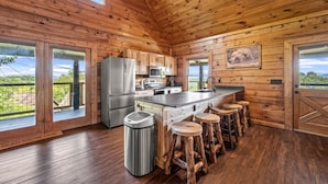A wooden cabin kitchen with a large island, stainless steel appliances, and a view of the outdoors. - Mountain View - Hot Tub - Game Room - Pool (Sevierville)