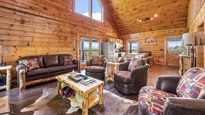 A cozy log cabin interior with a wooden ceiling, a large window, a dining area, and a kitchen. - Mountain View - Hot Tub - Game Room - Pool (Sevierville)