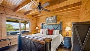A wooden cabin bedroom with a bed, two bedside tables, a ceiling fan, and a window with a view. - Mountain View - Hot Tub - Game Room - Pool (Sevierville)