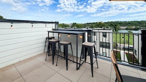 Terraza en la azotea con zona de bar, tres taburetes y vistas a un río y vegetación.
