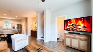 Una sala de estar moderna con una mesa de centro de madera, un sofá blanco y un televisor que muestra una chimenea.
