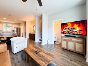 Ein stilvolles Wohnzimmer mit Couchtisch aus Holz, weißem Sofa und einem Fernseher, der einen Kamin zeigt.