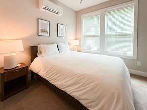 A bedroom with a bed, two bedside lamps, a nightstand, and a window with blinds.