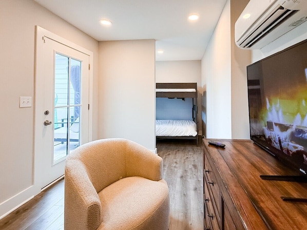 A room with a single bed, a television, a chair, and an air conditioning unit.