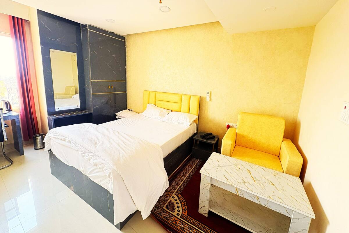 A hotel room with a bed, a bedside table, a chair, a desk, and a mirror.