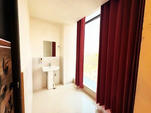 A bathroom with a sink, mirror, and a window with red curtains. - Hotel Ranjana Palace (Purnia)