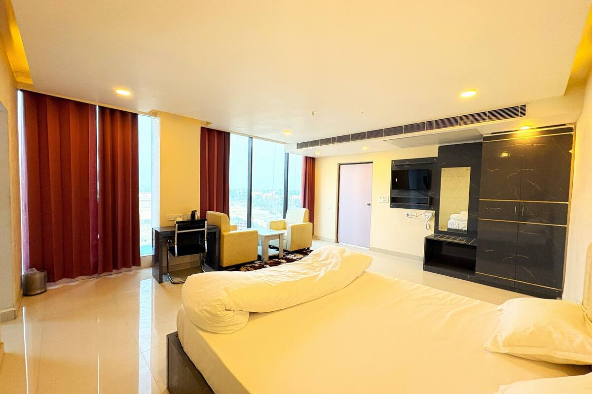 A hotel room with a large bed, a desk with a chair, a TV, and a wardrobe.