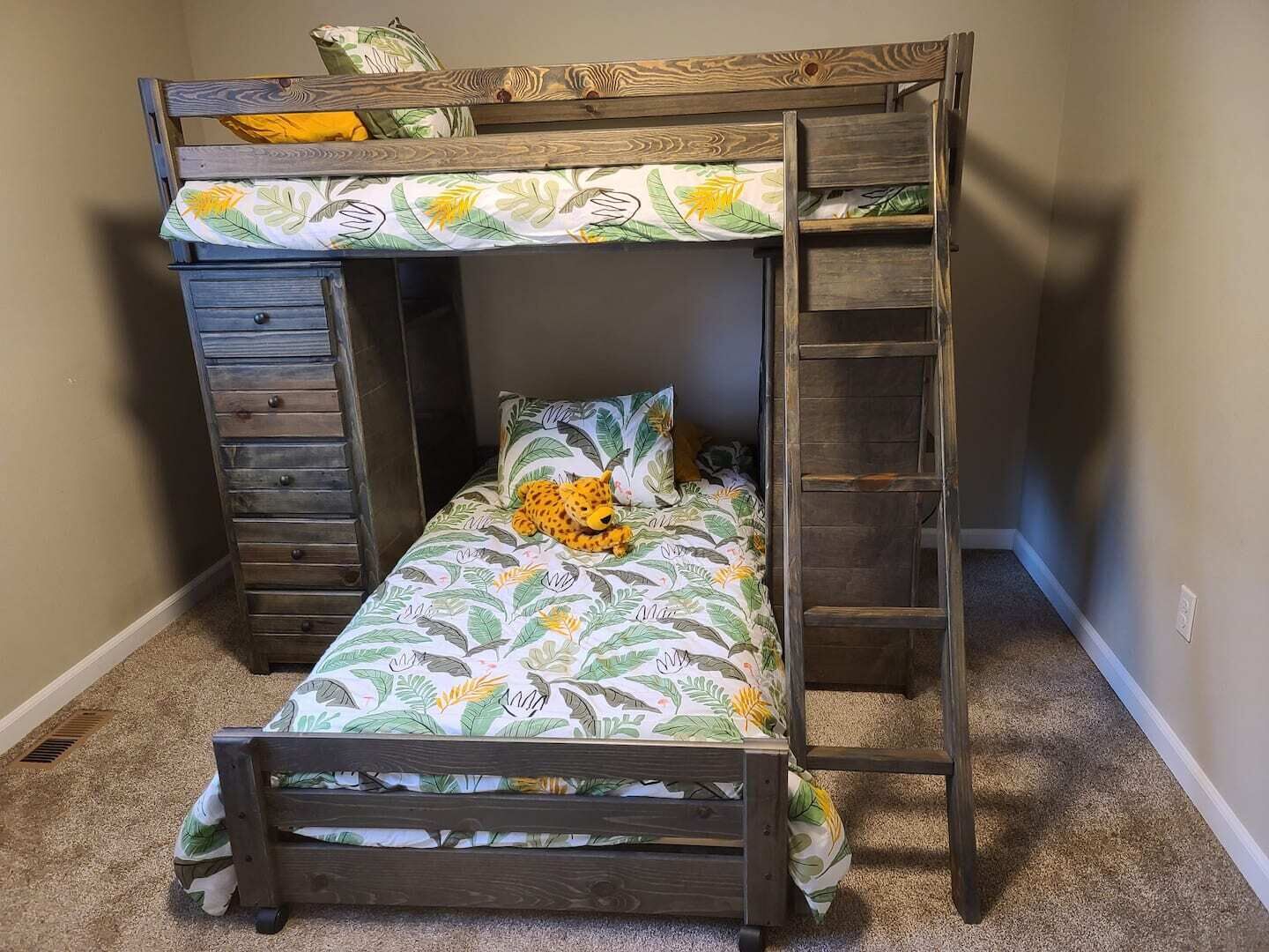 Ein Etagenbett mit Blumenmusterdecke, einer kleinen Leiter und einer Schubladenkommode.