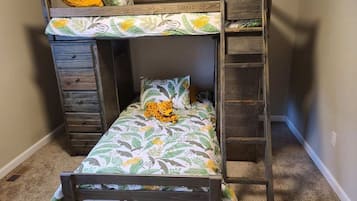 Ein Etagenbett mit Blumenmusterdecke, einer kleinen Leiter und einer Schubladenkommode.