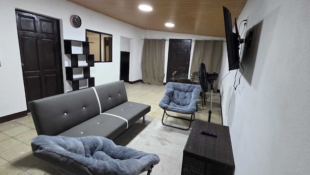 A living room with a sofa, armchair, and a TV mounted on the wall.