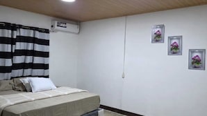 A bedroom with a bed, black and white striped curtains, an air conditioning unit, and three framed pictures on the wall.